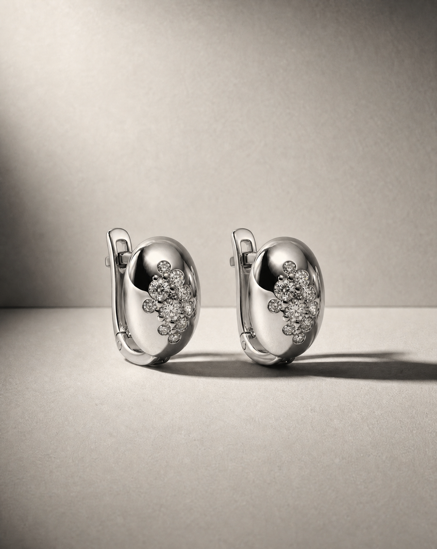 A pair of polished silver hoop earrings with clusters of small diamonds, displayed on a neutral gray surface against a matching gray background.