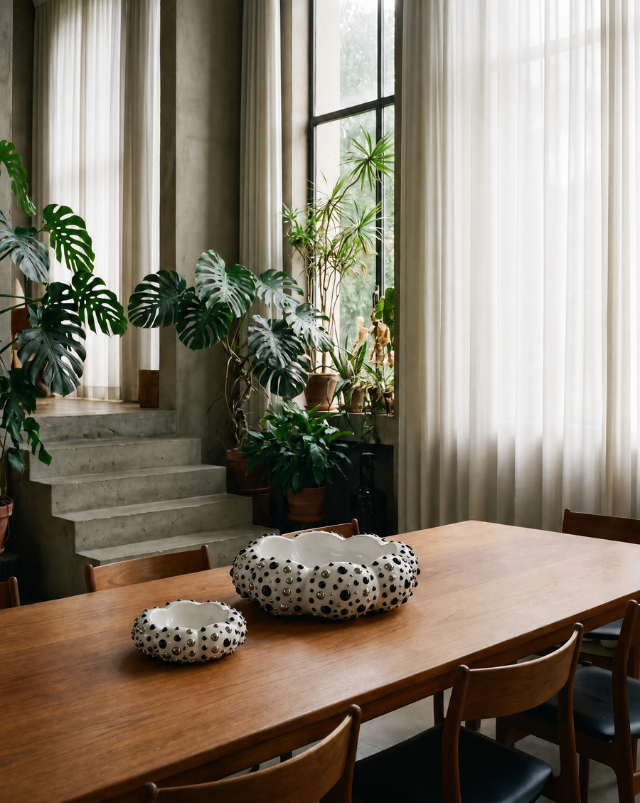 A styled dining room scene featuring a wooden dining table with two black-and-white speckled resin bowls, 