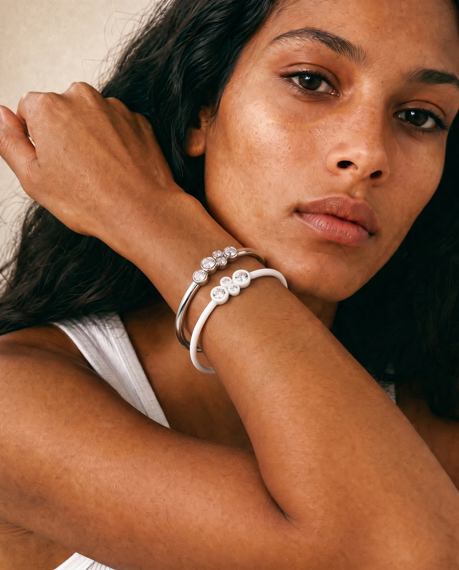 A close-up lifestyle shot of a woman wearing  a silver and white resin pair of bangles set with bezel diamonds 
